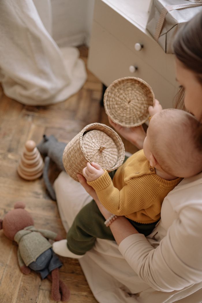 A mother and baby bond while playing with wooden and woven toys on a wooden floor, creating a warm family moment.